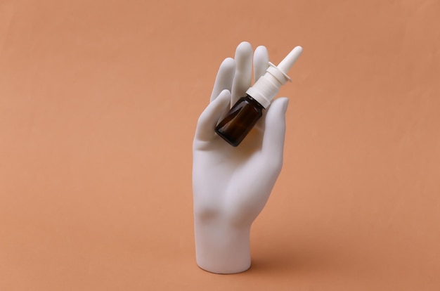 Mão de manequim branco segurando spray nasal em fundo marrom