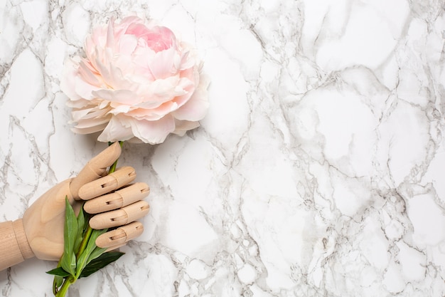 Mão de manequim de madeira com flor piony na superfície de mármore