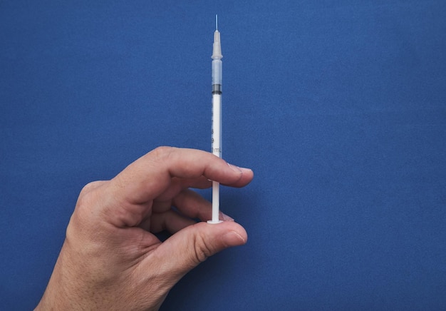 Mão de médico segurando seringa para vacinar com fundo azul e espaço para cópia