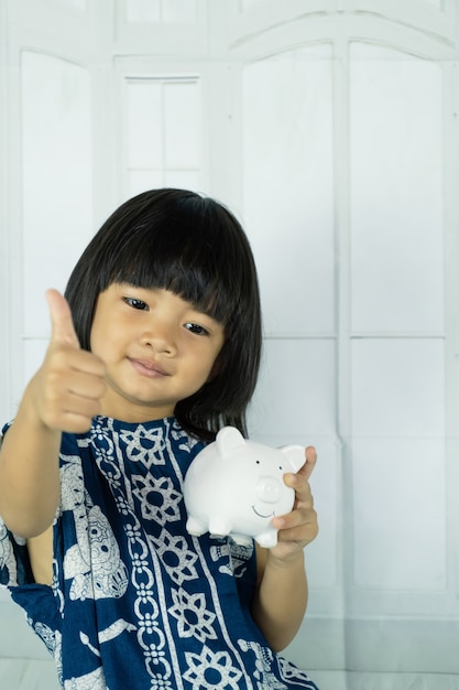 Mão de menina asiática segurando o cofrinho branco, aprenda a economizar para o conceito de futuro.