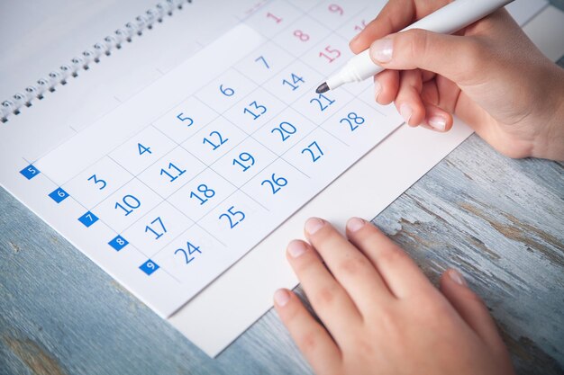 Mão de menina marca o calendário com um marcador