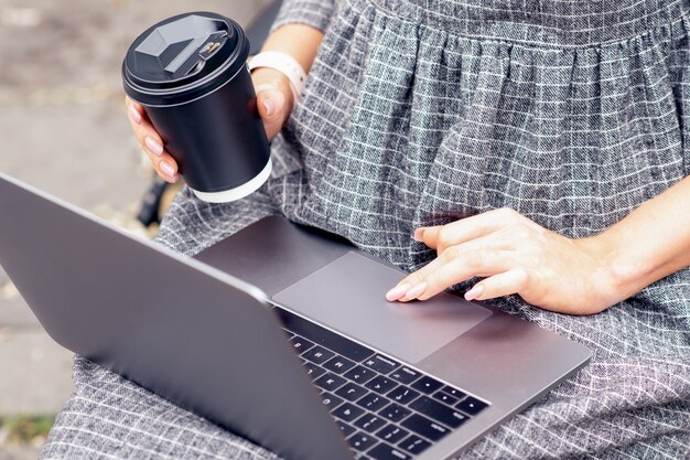 Mão de menina usando laptop enquanto segura uma xícara de café