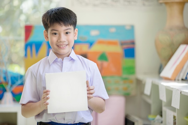 Mão de menino asiático feliz segurando a placa de papel em branco e olhando para a câmera