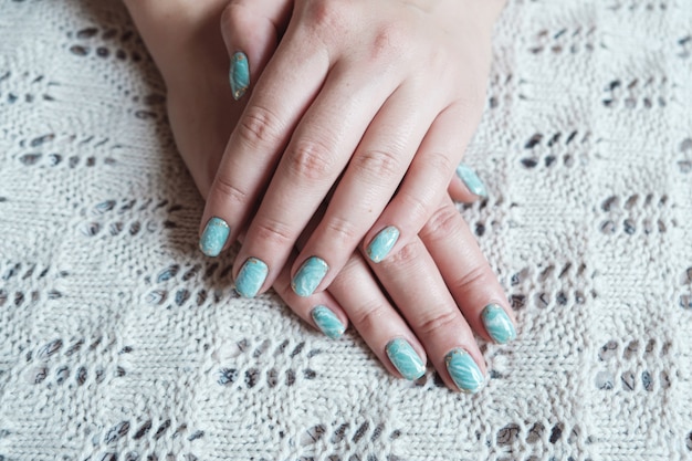 Mão de modelo de mulher mostrando manicure pastel verde mármore com folha de ouro nas unhas curtas