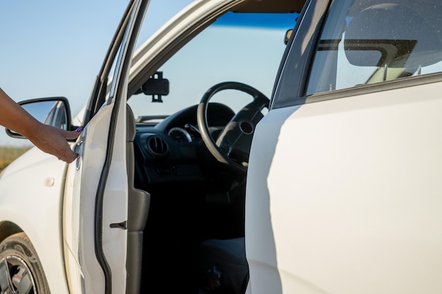 Mão de mulher abrindo a porta de um carro branco lançando uma sombra sobre ele na hora do nascer do sol