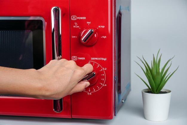 Mão de mulher ajustando o tempo com botão de círculo para aquecer comida de microondas na cozinha.