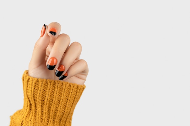 Mão de mulher bem cuidada em fundo branco desenho de unhas laranja na moda