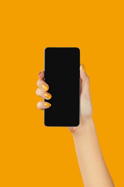 Mão de mulher bem cuidada segurando smartphone preto com tela em branco em fundo laranja