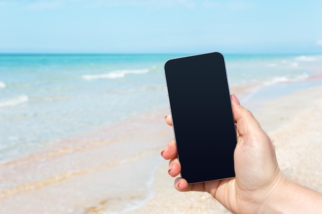 Mão de mulher bonita usando telefone inteligente na praia