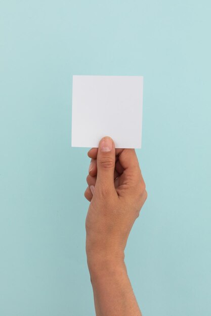 Foto mão de mulher caucasiana segurando papel branco sobre fundo azul pálido. espaço de cópia de mensagem de saudações.