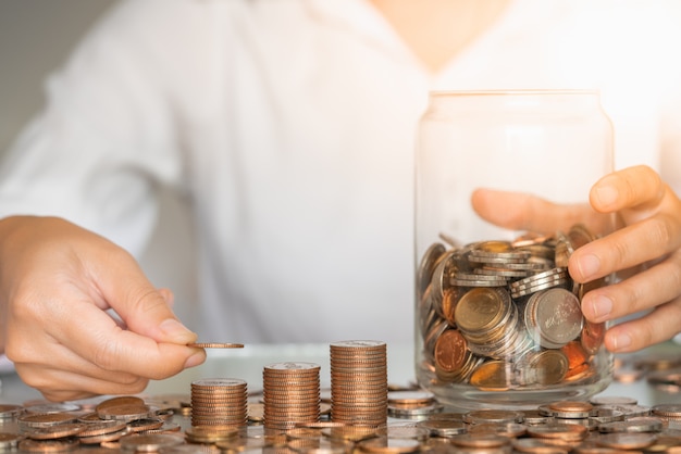 Foto mão de mulher closeup colocando moedas na pilha com frasco de vidro na mesa. conceito de dinheiro de negócios e poupança.