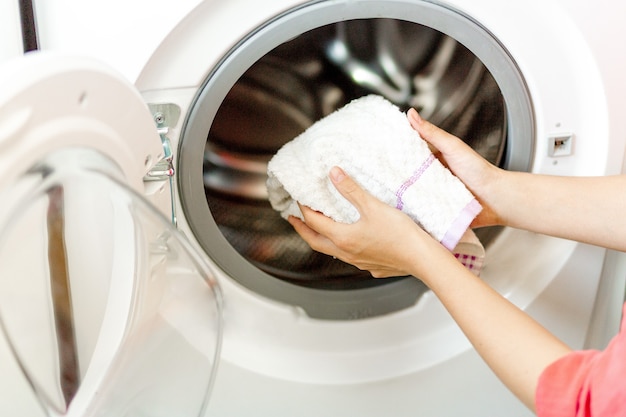 Mão de mulher colocar uma toalha branca na máquina de lavar. Lavanderia de trabalho dona de casa em casa.