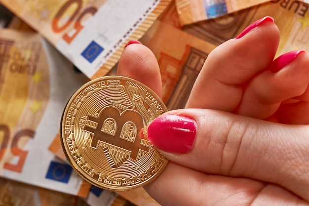 Mão de mulher com bitcoin e notas de 50 e cinquenta euros de notas de fundo