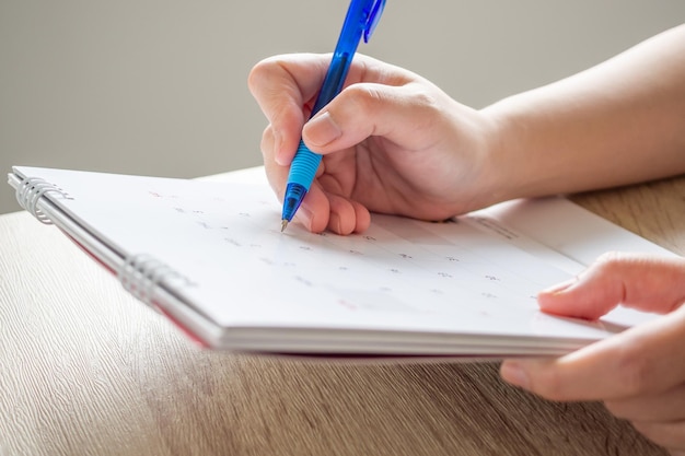 Mão de mulher com caneta escrevendo na data do calendário conceito de reunião de planejamento de negócios