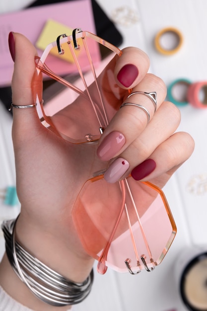 Mão de mulher com design minimalista de primavera rosa verão manicure segurando óculos de sol