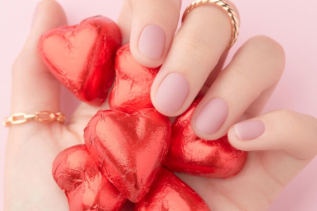 Mão de mulher com manicure rosa matte de moda segurando doces em close-up