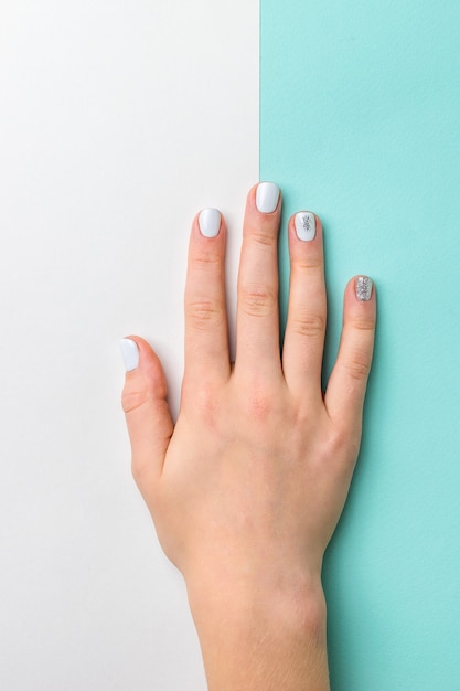 Mão de mulher com maquiagem leve elegante em fundo branco e azul. cuidado com as mãos.