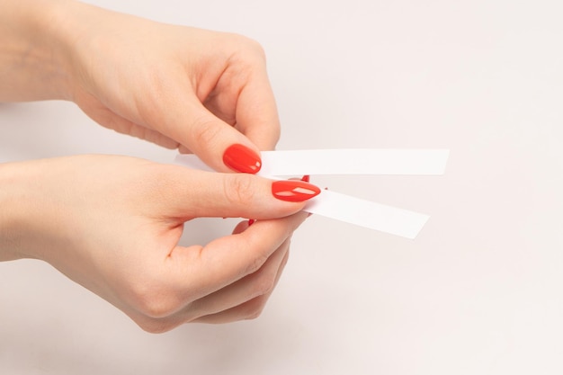 Mão de mulher com unhas vermelhas com tiras de teste para o perfume isolado em um fundo branco