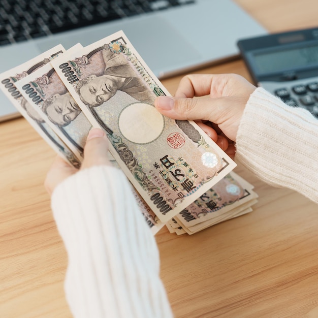 Mão de mulher contando notas de ienes japoneses com calculadora dinheiro de mil ienes japão dinheiro recessão de impostos economia inflação salário de financiamento de investimentos e conceitos de pagamento