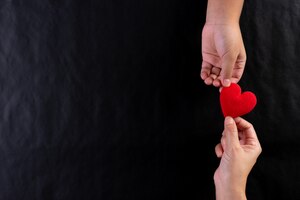 Mão de mulher dando coração vermelho para criança. dia internacional do conceito de caridade. copie o espaço.