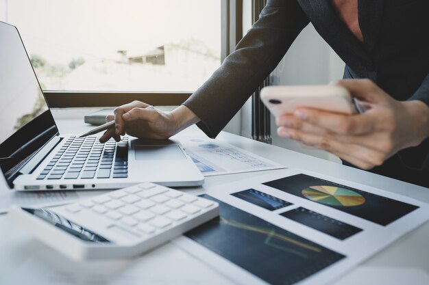 Mão de mulher de negócios segurando smartphone, análise do gráfico com calculadora e laptop no escritório em casa para definir metas de negócios desafiadoras