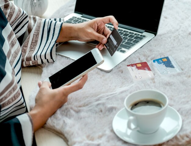 Mão de mulher de negócios segurando um cartão de crédito para fazer compras online em casa, gastando dinheiro com o smartphone