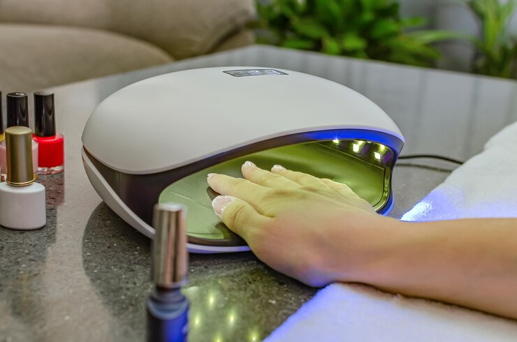 Foto mão de mulher dentro da lâmpada de prego em close-up da mesa. lâmpada uv para secagem de unhas pelo método de gel. unhas roxas secas em uma lâmpada.