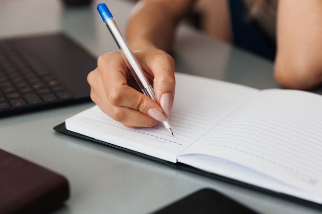 Mão de mulher escrevendo com uma caneta em um caderno