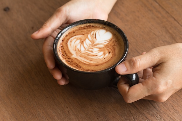 Mão de mulher está segurando Piccolo Latte art em um copo no topo lindo coração