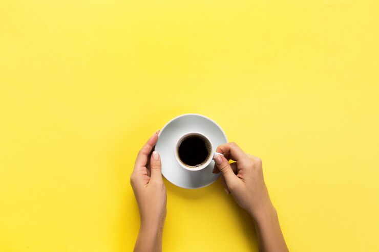 Foto mão de mulher estilo minimalista segurando uma xícara de café sobre fundo amarelo. vista plana leiga