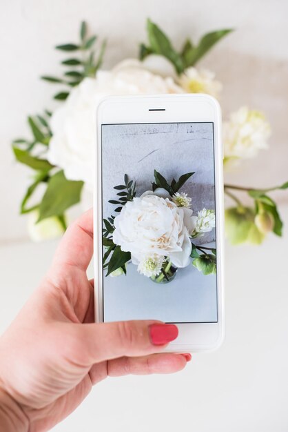 Mão de mulher fotografando flores brancas com câmera de smartphone