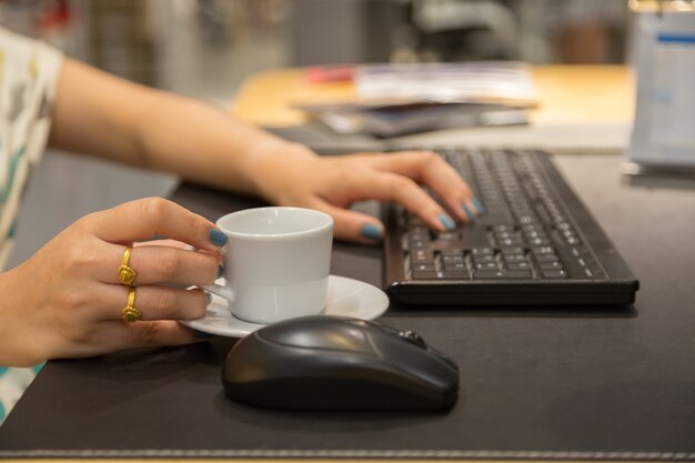 Mão de mulher holdding xícara de café com fundo de mesa de trabalho