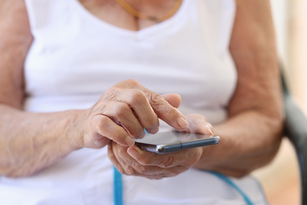 Mão de mulher idosa com mensagens de smartphone em casa conversando e usando smartphone na aposentadoria