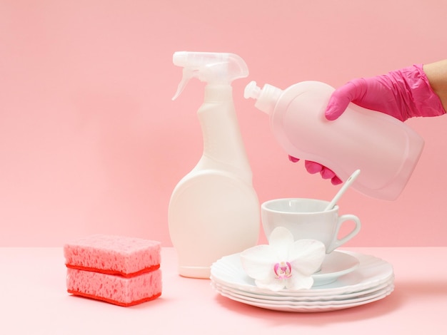 Mão de mulher na luva protetora com garrafa de detergente em um fundo rosa