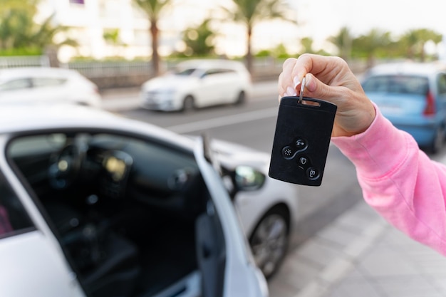 Mão de mulher segurando a chave do cartão por veículo branco com porta aberta Conceitos de carona de aluguel de carros