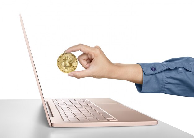 Mão de mulher segurando bitcoin dourado na frente de um laptop