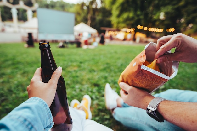 Mão de mulher segurando garrafa de cerveja mão de homem segurando batatas fritas cinema ao ar livre