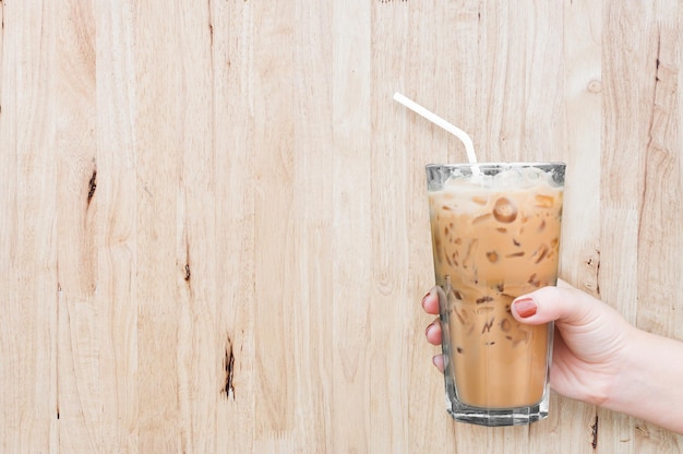 Mão de mulher segurando o café gelado de vidro no fundo de madeiraCafé com leite gelado