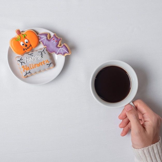 Mão de mulher segurando uma xícara de café durante comer biscoitos engraçados de Halloween Feliz dia de Halloween Truque ou Ameaça Olá outubro outono outono Festa tradicional e conceito de férias