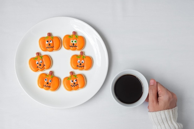 Mão de mulher segurando uma xícara de café durante comer biscoitos engraçados de Halloween Feliz dia de Halloween Truque ou Ameaça Olá outubro outono outono Festa tradicional e conceito de férias