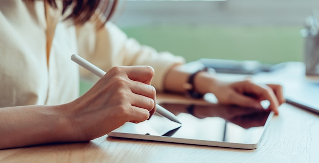 Mão de mulher trabalhando no tablet e pressione o laptop em cima da mesa no escritório.