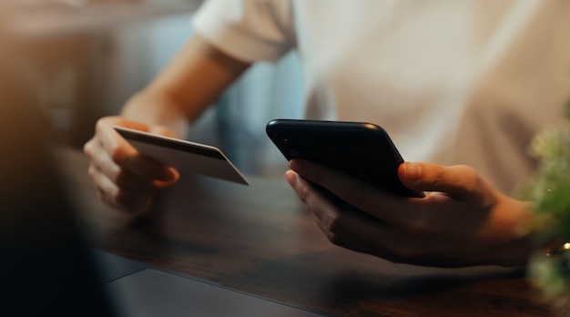 Mão de mulher usando smartphone e segurando o cartão de crédito com pagamento on-line no celular.