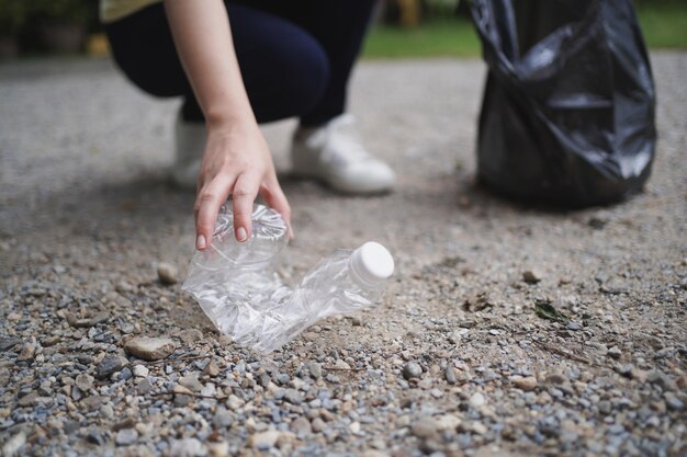 Mão de mulher voluntária de caridade segurando saco preto de lixo e lixo de garrafa de plástico para reciclagem para limpeza no conceito de voluntariado do parque, reutilização e ajuda voluntária