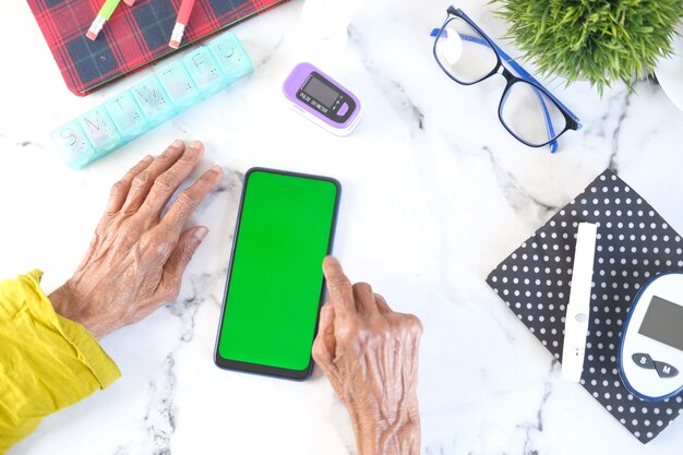 mão de mulheres idosas usando um telefone inteligente na mesa com ferramentas de medição de diabetes