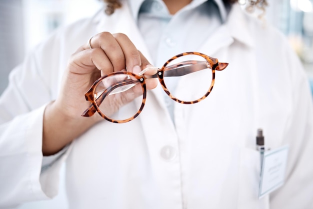 Mão de óculos e visão com uma médica segurando um par de óculos de armação em uma clínica para correção da visão Saúde médica e seguros com uma optometrista feminina mostrando lentes de prescrição