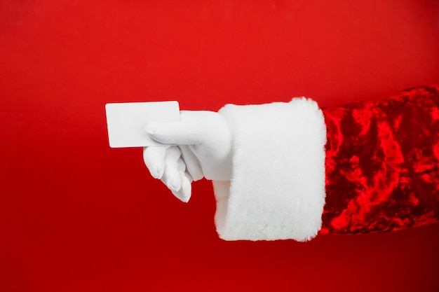 Foto mão de papai noel segurando um cartão de crédito de plástico em branco no vermelho