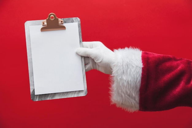 Mão de Papai Noel segurando uma prancheta com página em branco