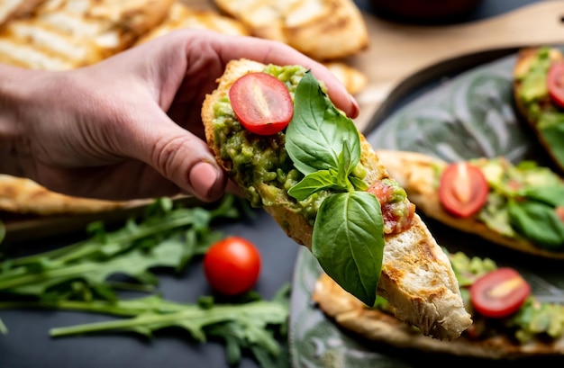 Mão de pessoa segurando torradas bruschetta com manjericão guacamole e lanche mexicano de tomate cereja