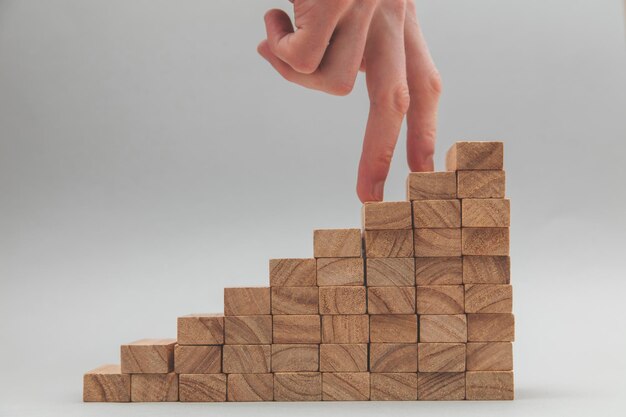 Mão de pessoas subindo um conjunto de blocos de madeira Desenvolvimento de negócios e conceito de crescimento