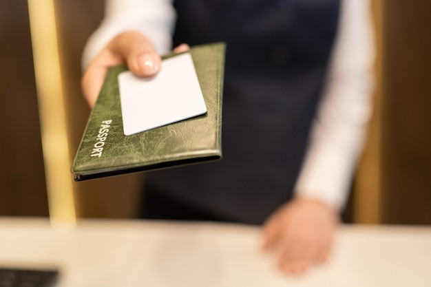 Mão de recepcionista passando passaporte e cartão de plástico branco em branco